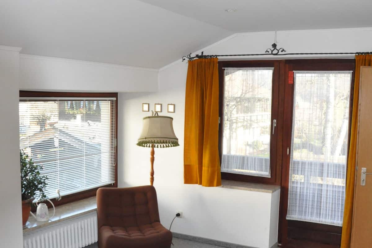 A bedroom with a bed, a chair, a lamp, and a window with curtains.