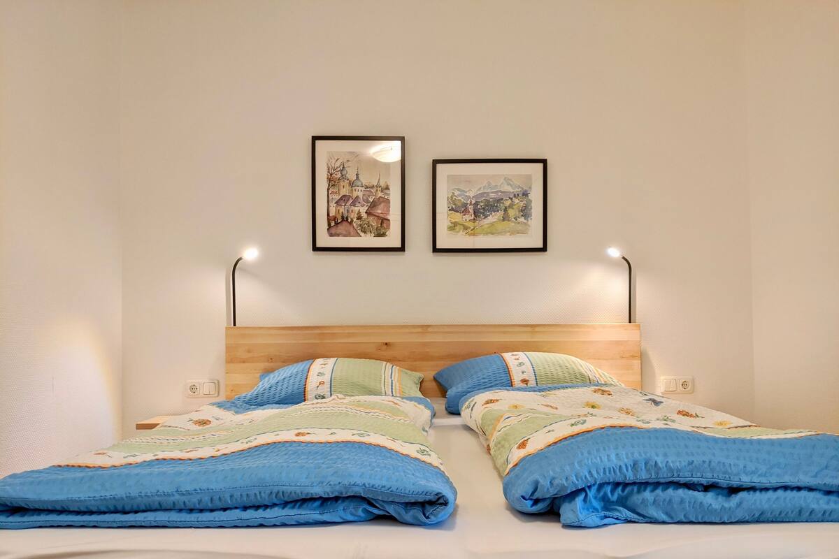A double bed with a wooden headboard, two bedside lamps, and two framed pictures on the wall.