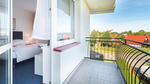 Un balcon avec une balustrade blanche, un lit avec une tête de lit rouge et une fenêtre avec des rideaux blancs.