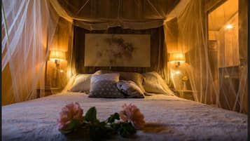 A bedroom with a canopy bed, two bedside lamps, and a floral arrangement on the bed.