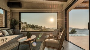 Ein modernes Wohnzimmer mit großem Fenster und Aussicht auf eine schöne Landschaft, einem Sofa, einem Couchtisch und zwei Sesseln.
