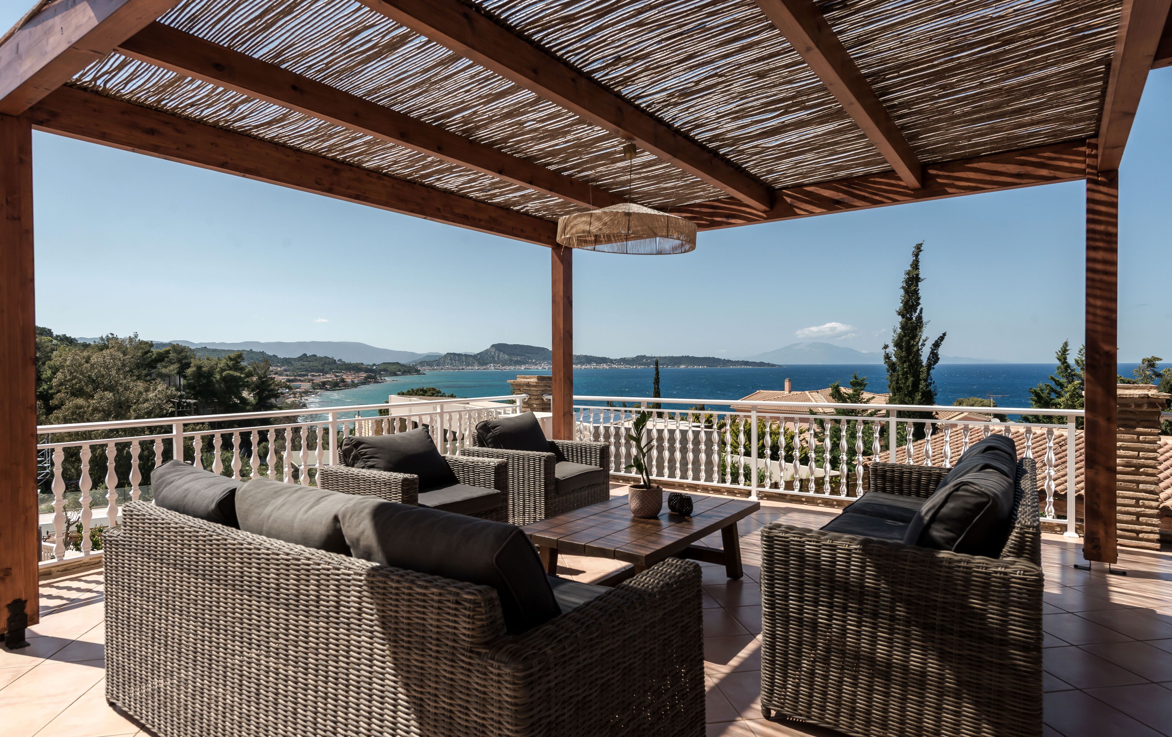 A covered outdoor seating area with wicker furniture and a view of the sea.