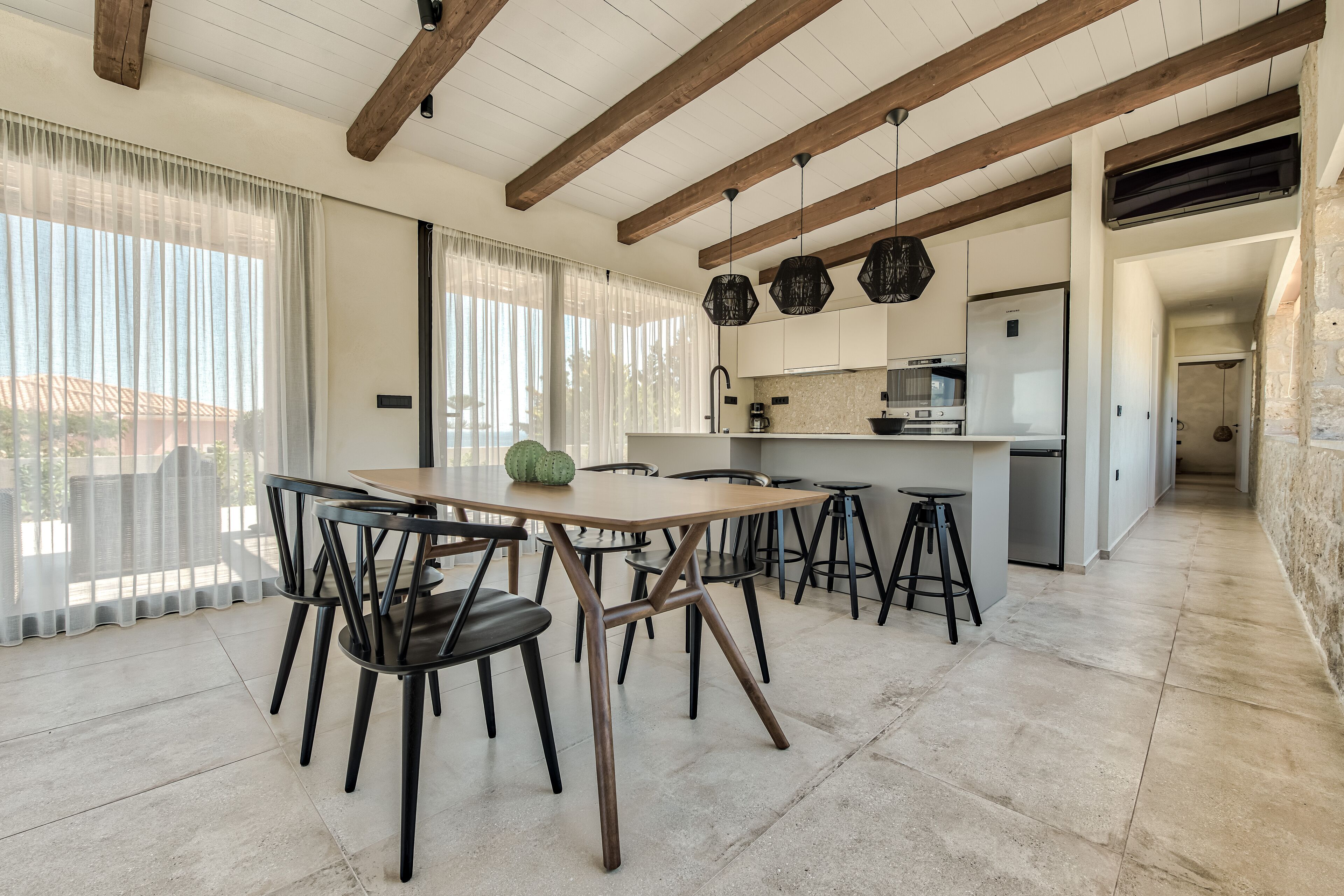 A modern kitchen with a central island, wooden beams on the ceiling, and a dining area with a table and chairs.