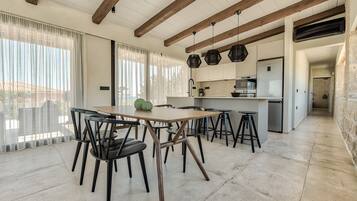 A modern kitchen with a central island, wooden beams on the ceiling, and a dining area with a table and chairs.