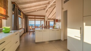 Eine moderne Küche mit einer großen Kochinsel, Holzbalken an der Decke und Blick ins Freie.