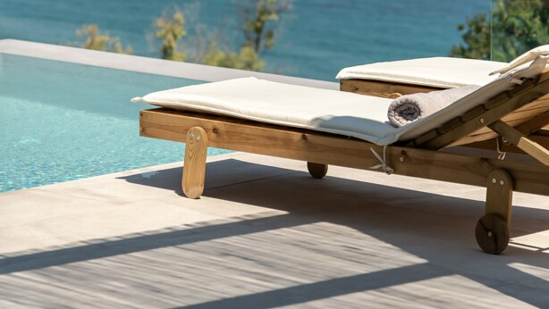 Ein Holz-Lounge-Sessel am Pool mit Blick auf das Meer und einen fernen Strand.