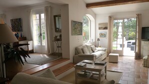 A spacious living room with a sofa, a coffee table, and a TV. There are large windows and a door leading outside. - Chambres d'hôtes de Vérédème (Pujaut)