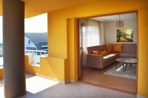 A modern living room with a sofa and a coffee table, a painting on the wall, and a view of the city through a balcony. - Ata Apart & Hotel (Bursa)