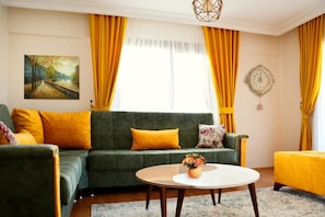 A living room with a green sofa, yellow cushions, a round coffee table with a vase, and a painting on the wall. - Ata Apart & Hotel (Bursa)