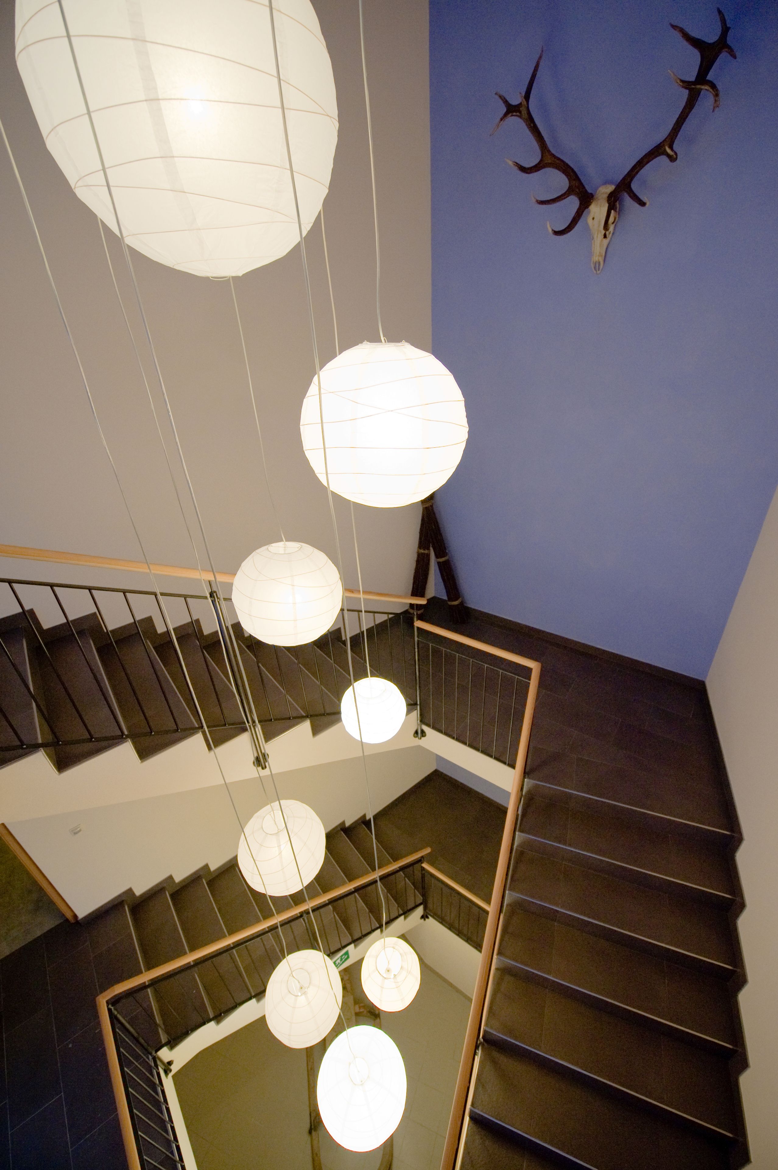 A staircase with a wooden railing and hanging spherical light fixtures.