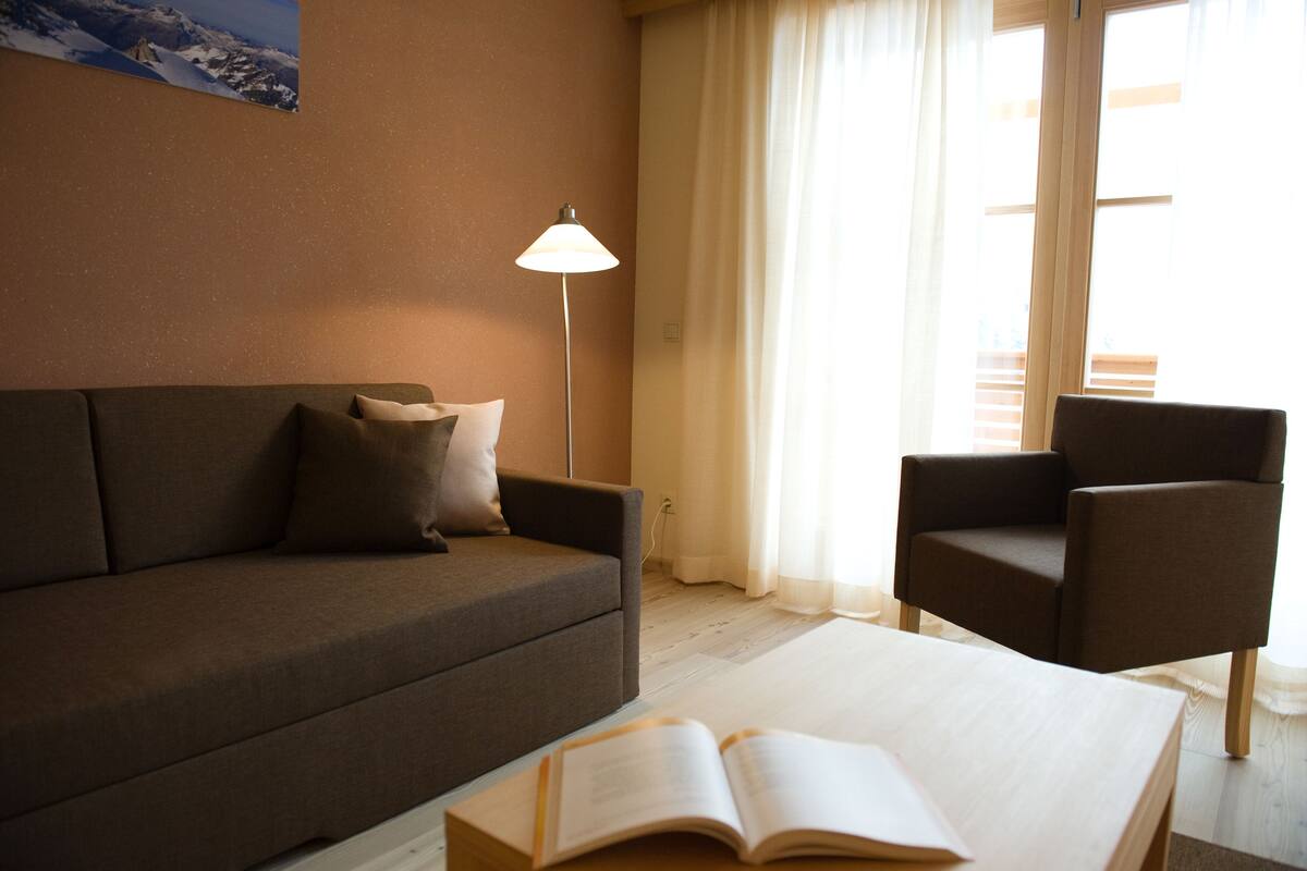 A cozy room with a brown sofa, a chair, and a table with an open book.