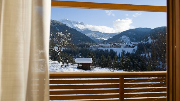 A view from a balcony with wooden railings, overlooking a snow-covered valley with mountains in the background. - Ostaria Posta (San Martino in Badia)