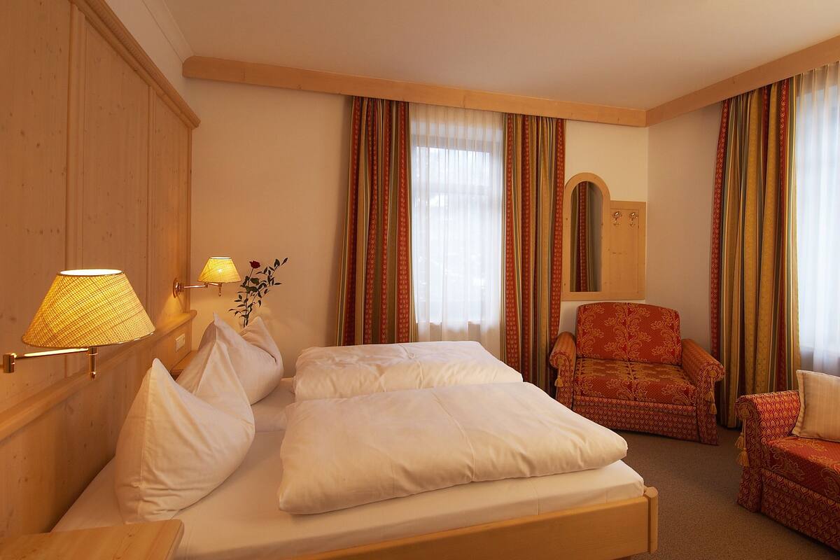 A hotel room with a bed, two chairs, a lamp, and a mirror.