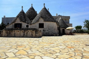 A stone building with multiple conical roofs, a paved courtyard, and a small outdoor seating area. - Masseria Peppeturro (Cisternino)