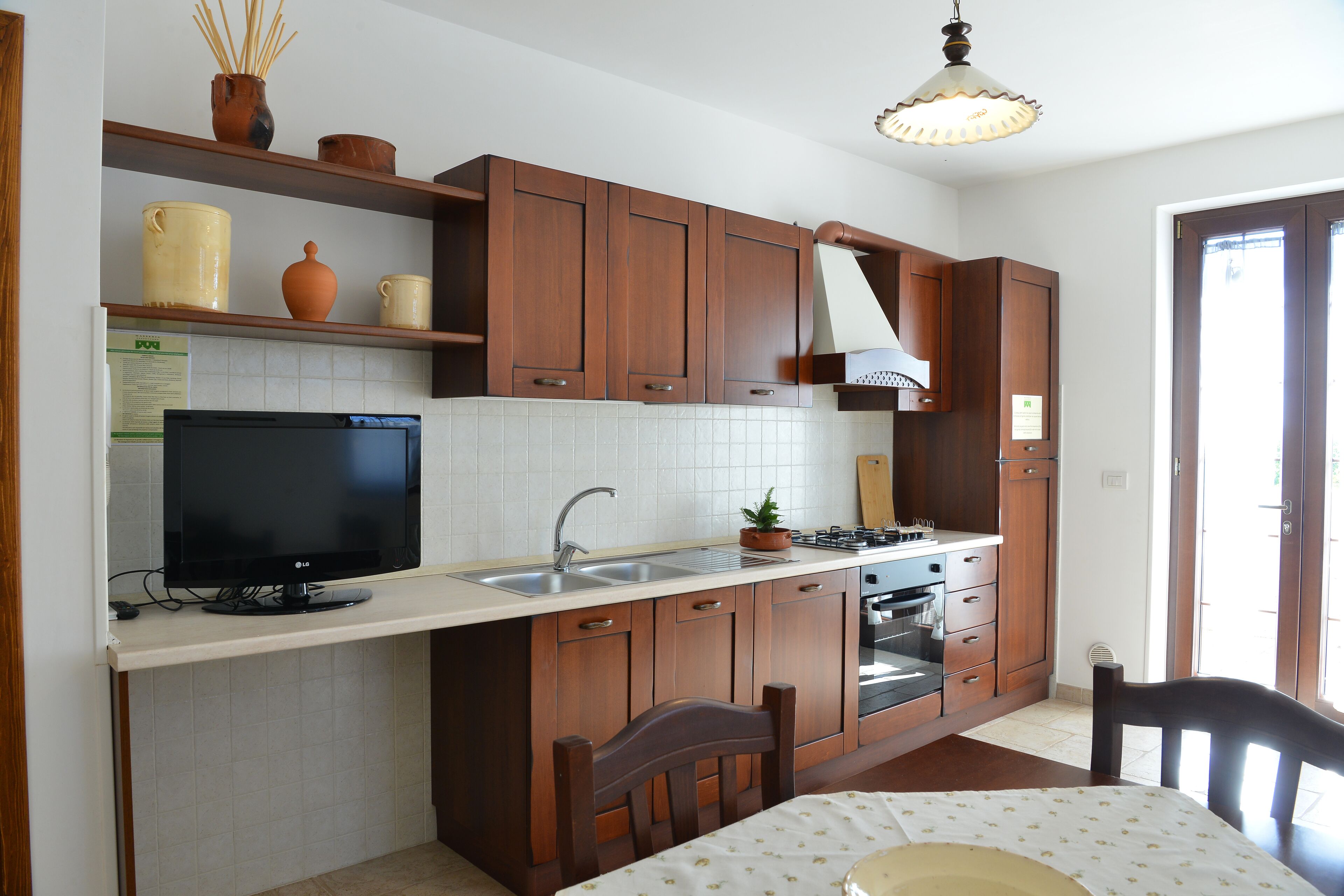 Una cocina con armarios de madera, horno empotrado, lavabo y televisor sobre una encimera.