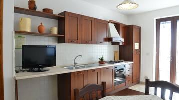 Una cocina con armarios de madera, horno empotrado, lavabo y televisor sobre una encimera.