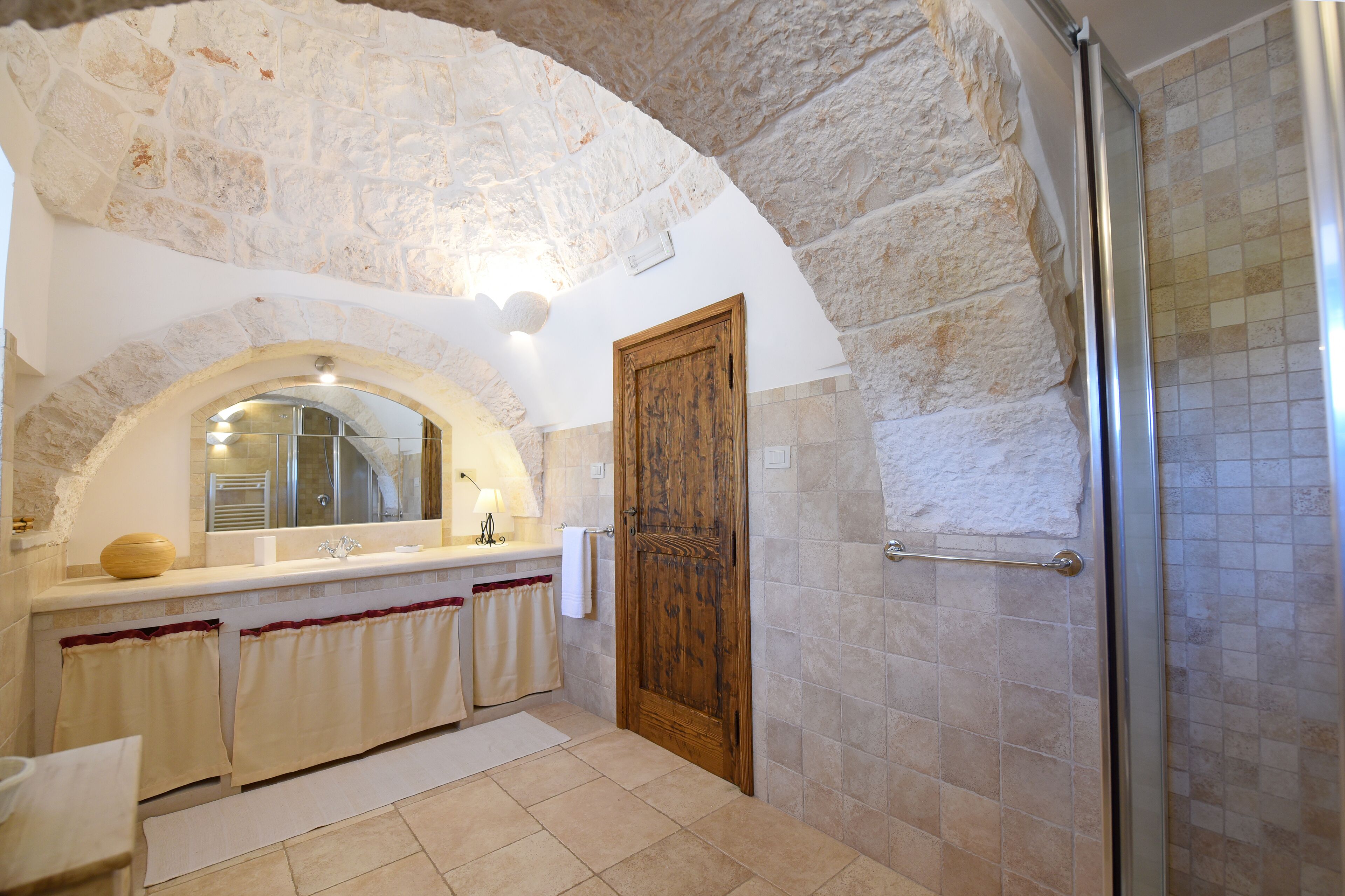 A bathroom with a stone arch, a wooden door, a shower, and a vanity with a mirror.