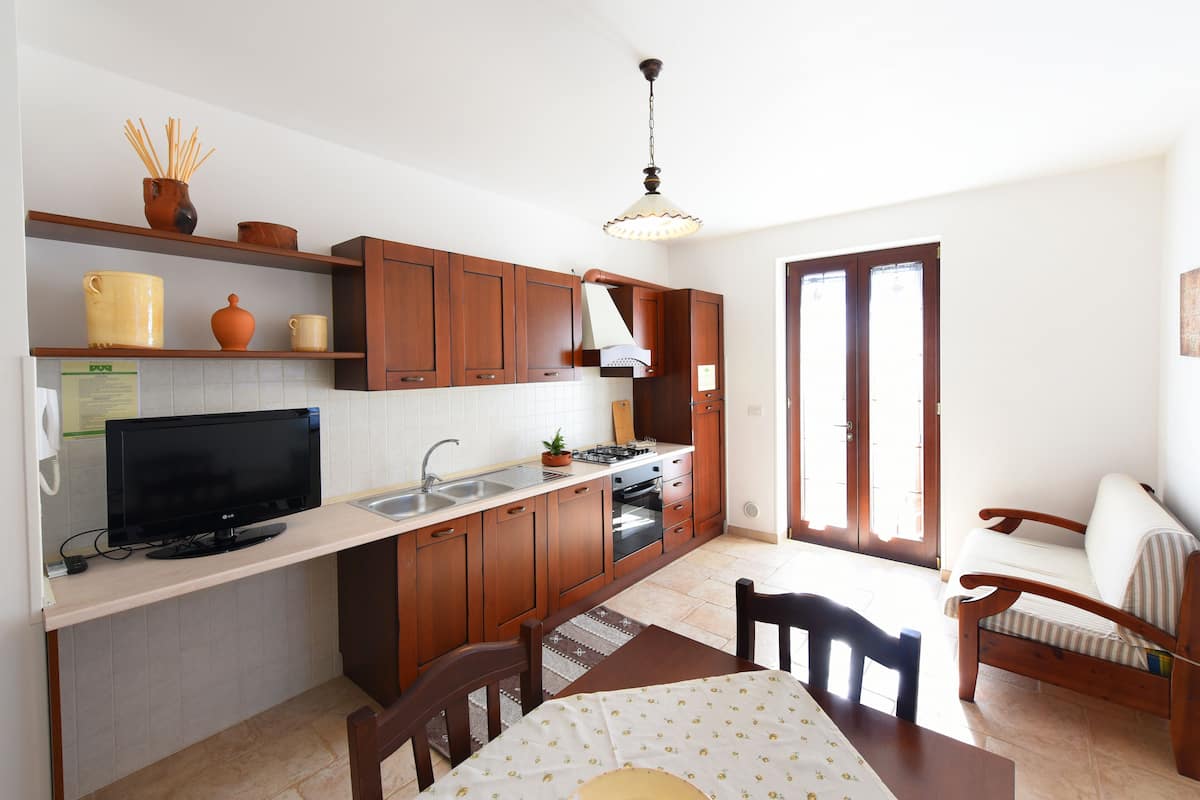 A compact kitchen with wooden cabinets, a built-in oven, a sink, and a television on a counter.