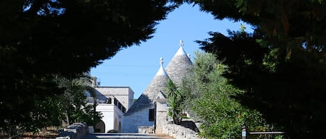 A stone pathway leading to a building with a conical roof, surrounded by trees and a stone wall.