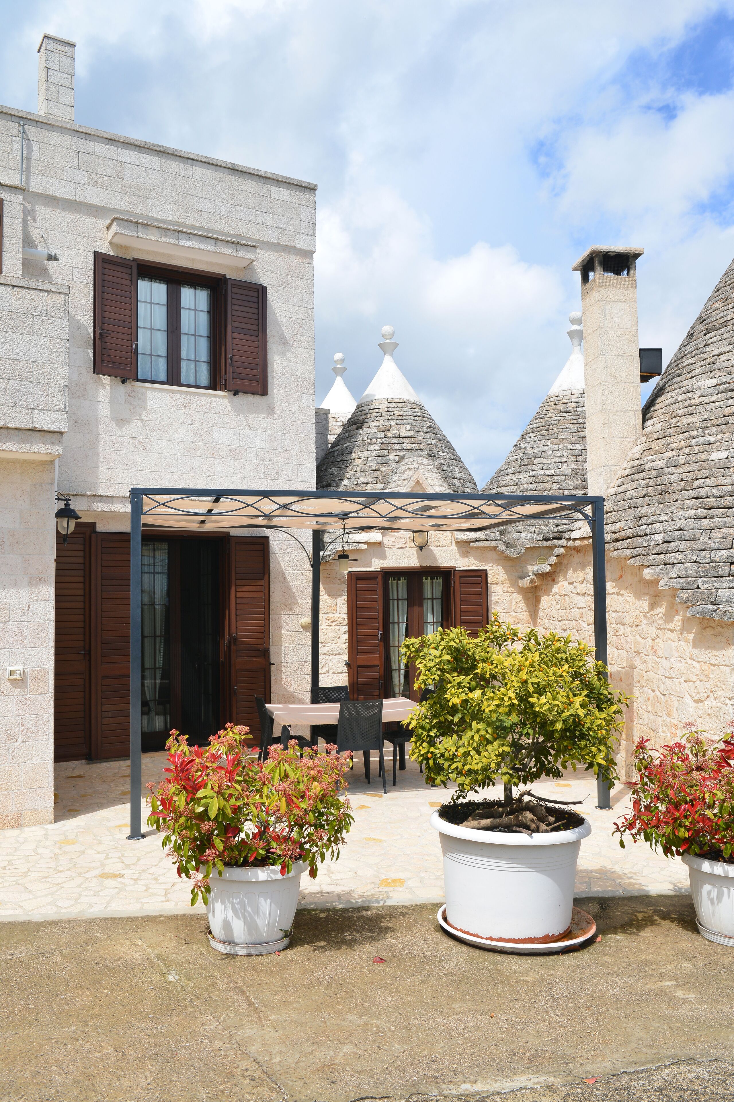 A courtyard with a covered seating area, potted plants, and stone buildings with conical roofs.