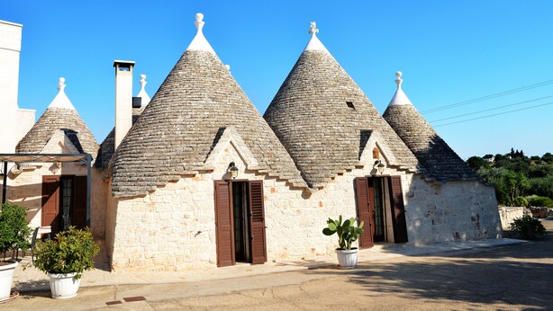 A row of stone buildings with conical roofs and wooden shutters. - Masseria Peppeturro (Cisternino)
