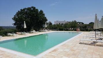 Una piscina rectangular con agua azul cristalina, rodeada por una solana con sillas de descanso y sombrillas.