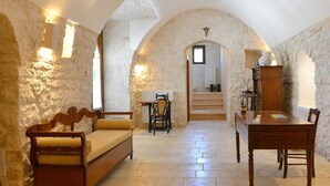 A room with a stone wall, a wooden sofa, a dining table, and a staircase leading to an upper level. - Masseria Peppeturro (Cisternino)
