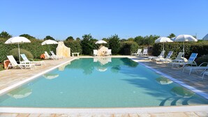 A swimming pool with lounge chairs and umbrellas, surrounded by greenery. - Masseria Peppeturro (Cisternino)
