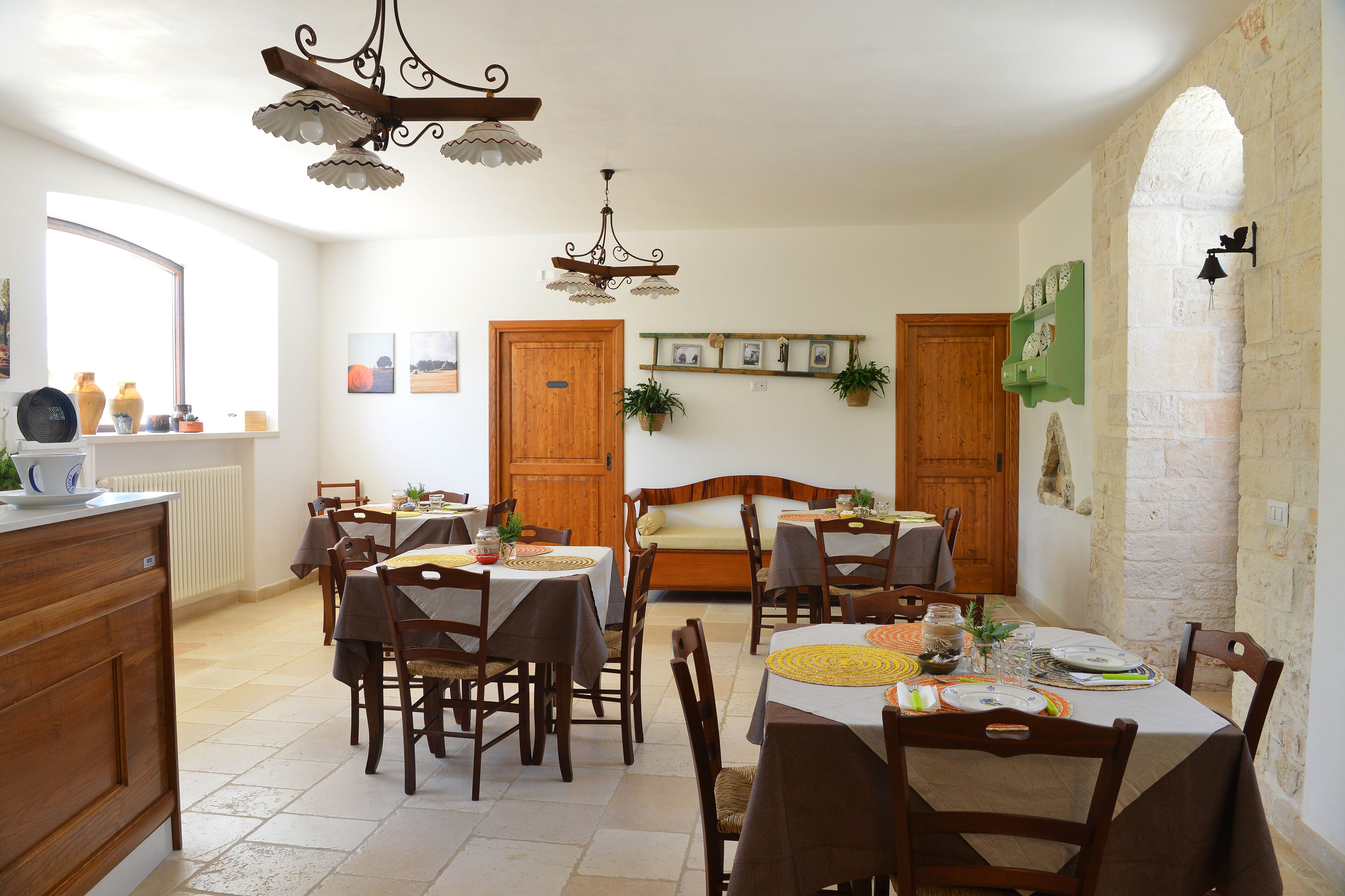 Un comedor con mesas y sillas de madera, una araña y una pared de piedra.