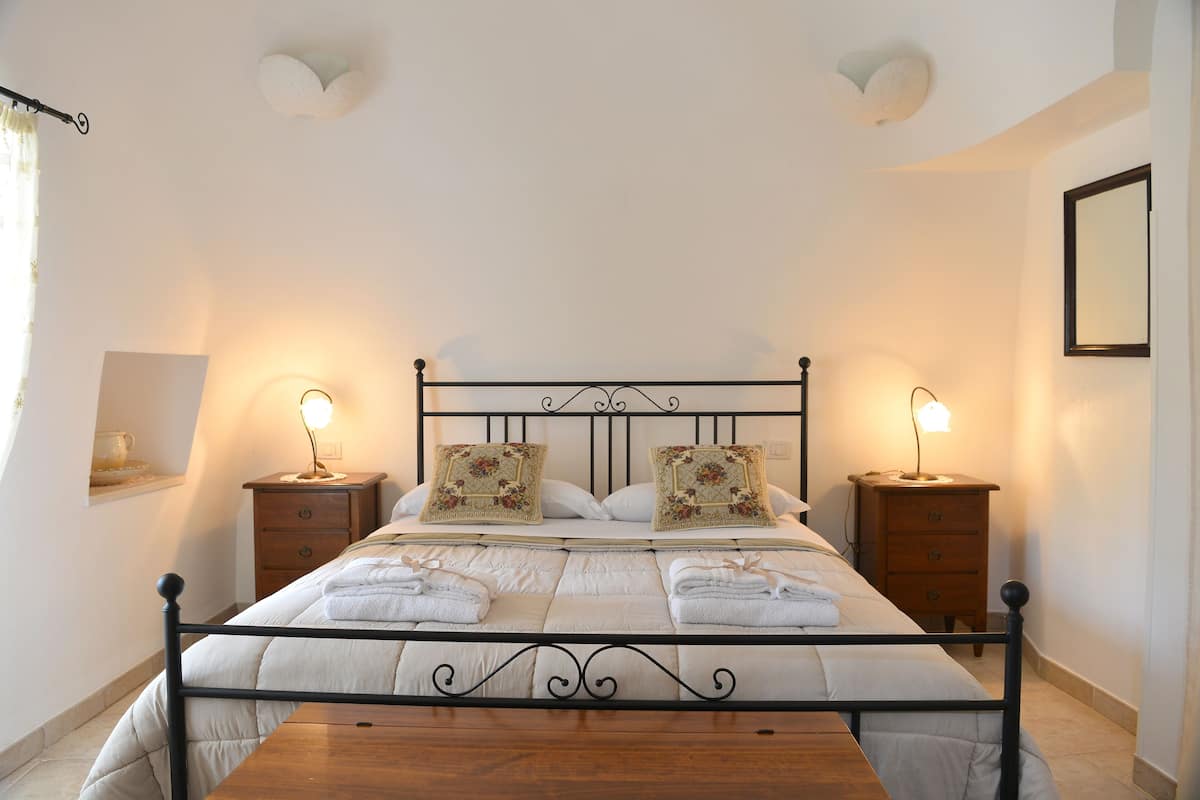 A neatly made bed with a metal frame, two bedside tables with lamps, and a mirror on the wall.