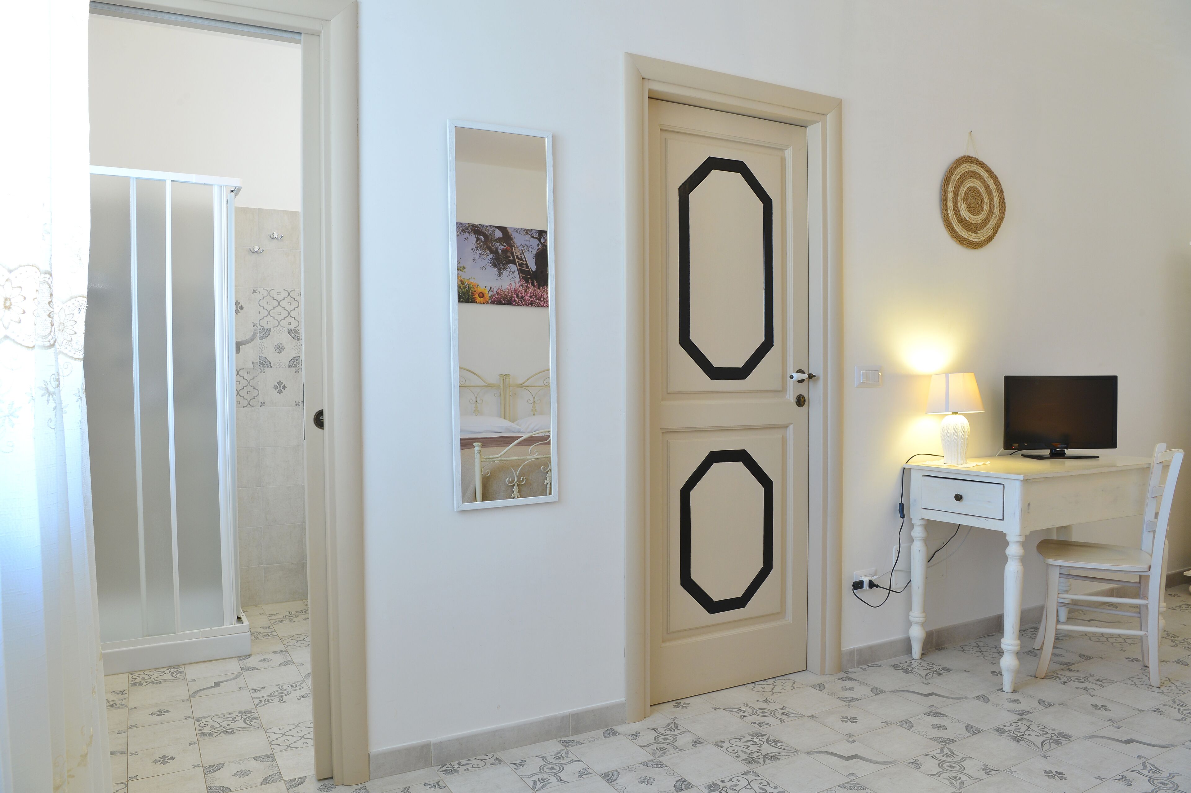 A room with a shower, a desk with a chair, a TV, and a wall-mounted mirror.