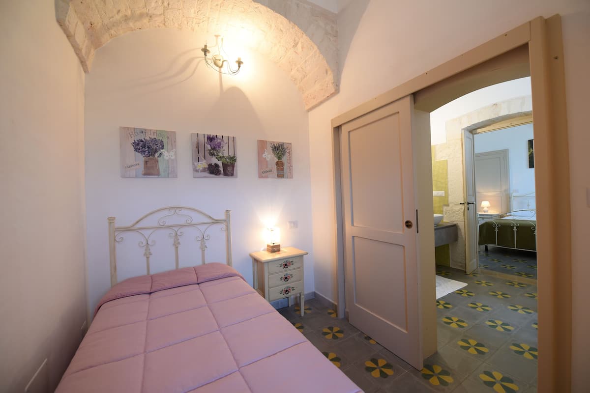 A bedroom with a bed, a nightstand, and a door leading to a bathroom.