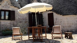 A stone building with conical roofs, a table with chairs, and an umbrella. - Masseria Peppeturro (Cisternino)