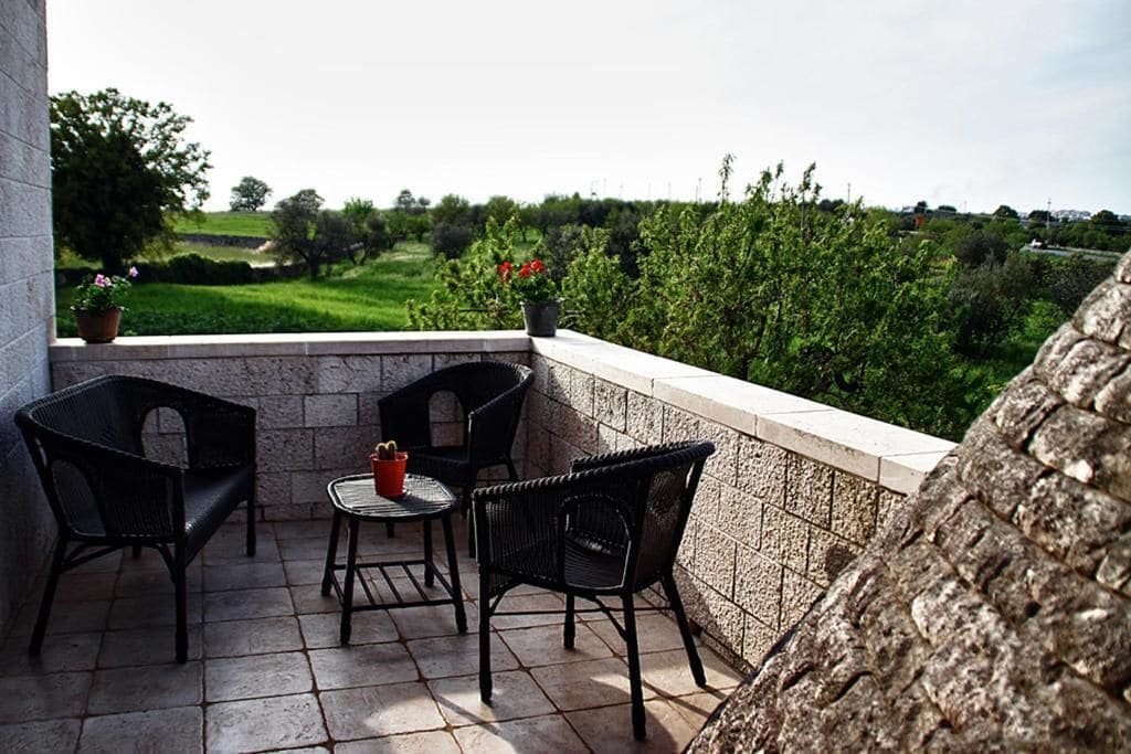 A balcony with two wicker chairs and a small table, overlooking a green landscape.