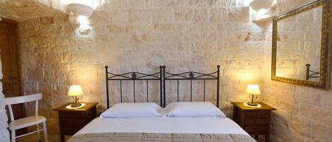 A bedroom with a stone wall, a bed with white bedding, two bedside tables with lamps, and a wooden chair.