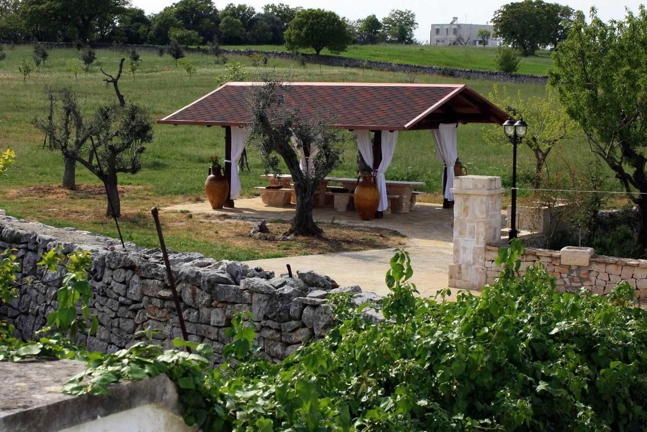 A stone wall, a pergola with a tiled roof, and a stone bench in a garden setting.