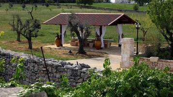 A stone wall, a pergola with a tiled roof, and a stone bench in a garden setting.