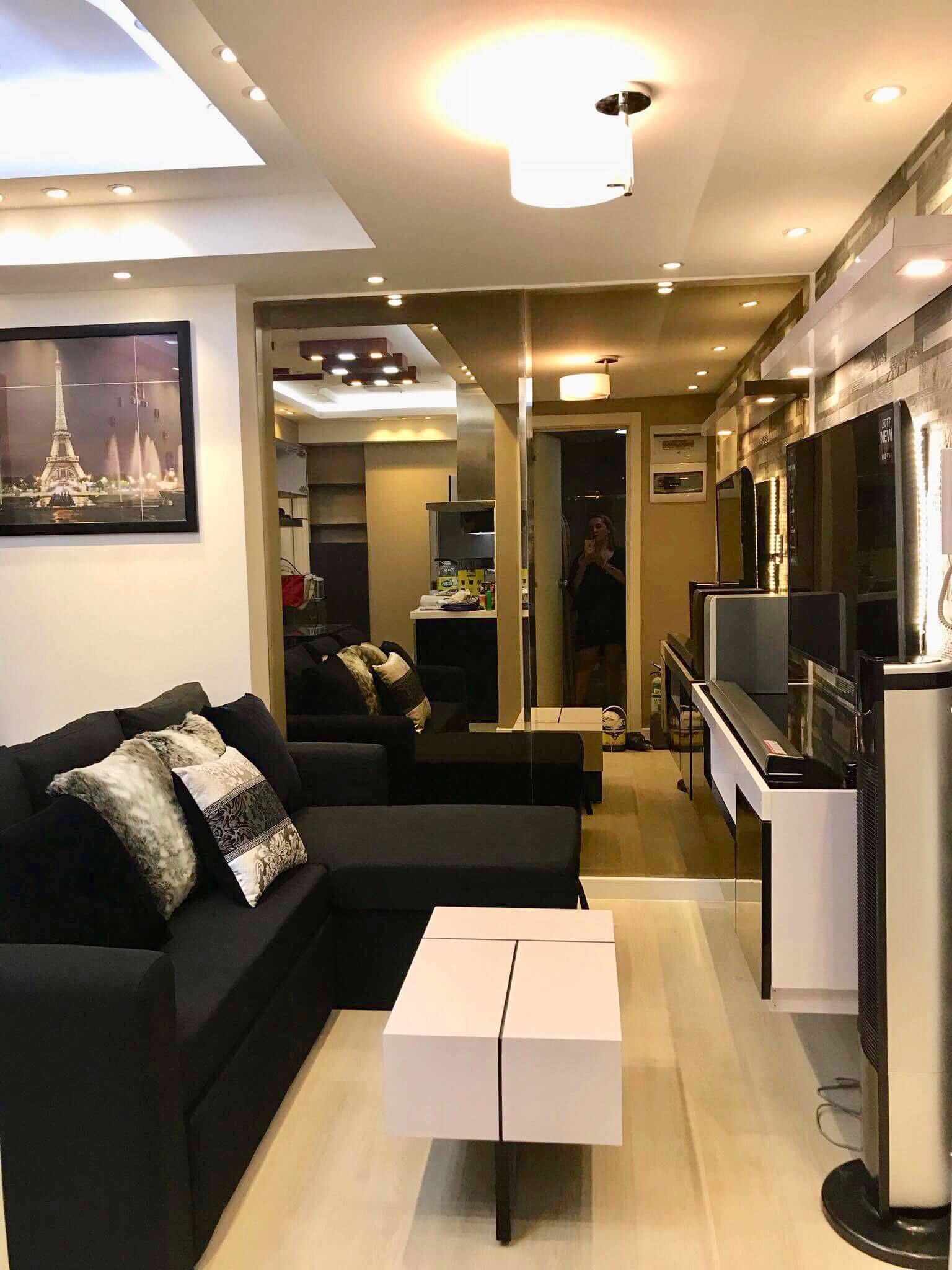 Un salon moderne avec un canapé noir, une table basse blanche et un téléviseur à écran plat.