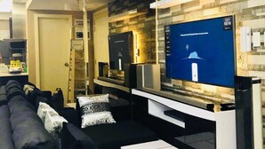 A modern living room with a flat-screen TV, a sofa, a coffee table, and a kitchen area in the background. - Maui 2 Bedroom Condo at Azure Urban Resort Residences (Parañaque)
