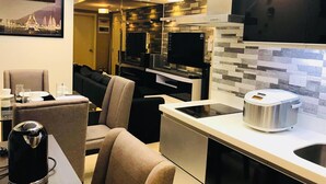 A modern kitchen with a built-in oven, a coffee maker, and a microwave. There is a dining area with a sofa and a table set for two. - Maui 2 Bedroom Condo at Azure Urban Resort Residences (Parañaque)