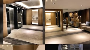 A modern hotel lobby with a reception desk, a seating area with a sofa, and a staircase leading to an upper floor. - Maui 2 Bedroom Condo at Azure Urban Resort Residences (Parañaque)