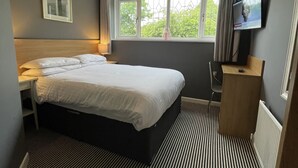A hotel room with a bed, a desk, a television, and a window with curtains. - Haymills Guesthouse (Solihull)
