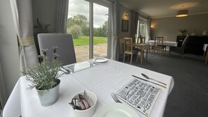 A dining area with a table set for two, a potted plant, and a menu. - Haymills Guesthouse (Solihull)