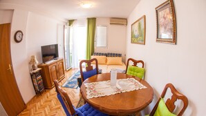 Un comedor con una mesa de madera, sillas con cojines azules y verdes, un televisor y un sofá al fondo.