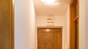 Un pasillo estrecho con una puerta de madera al final, una lámpara en el techo y una alfombra estampada en el suelo.
