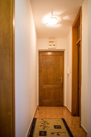A narrow hallway with a wooden door at the end, a light fixture on the ceiling, and a patterned rug on the floor. - City Apartments (Budva)