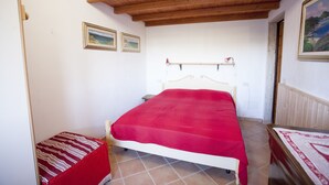 A bedroom with a wooden ceiling, a bed with a red blanket, a small bedside table, and a chair.