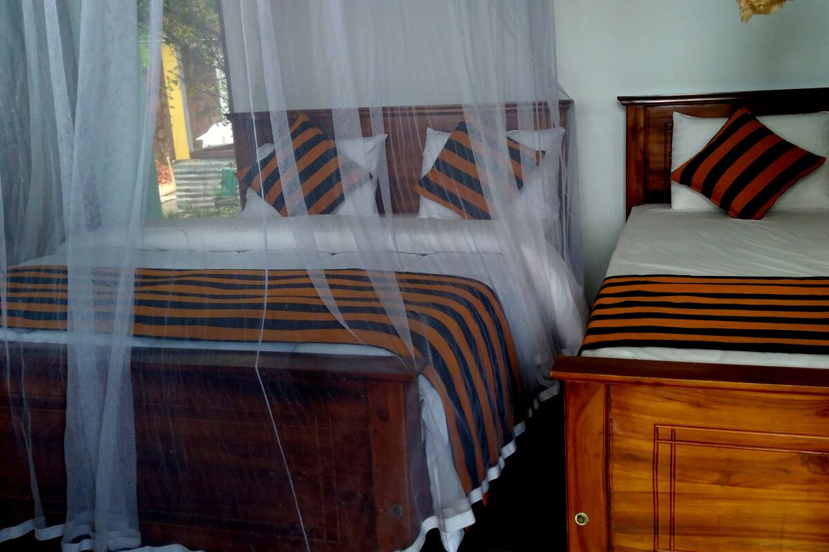 A double bed with striped bedding and a wooden headboard, a nightstand with a lamp, and a mosquito net over the window.