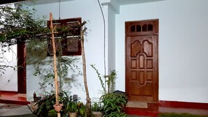 Un bâtiment blanc avec une porte et une fenêtre en bois, entouré de plantes en pot et d’un petit jardin.