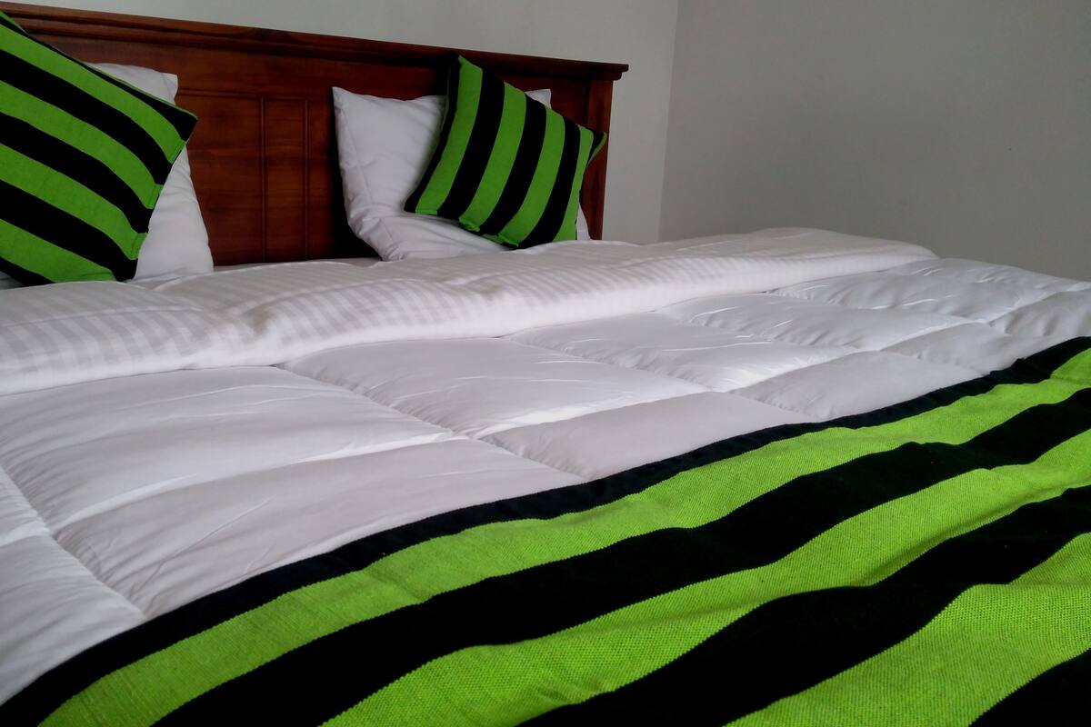 A neatly made bed with white bedding and a green and black striped blanket.